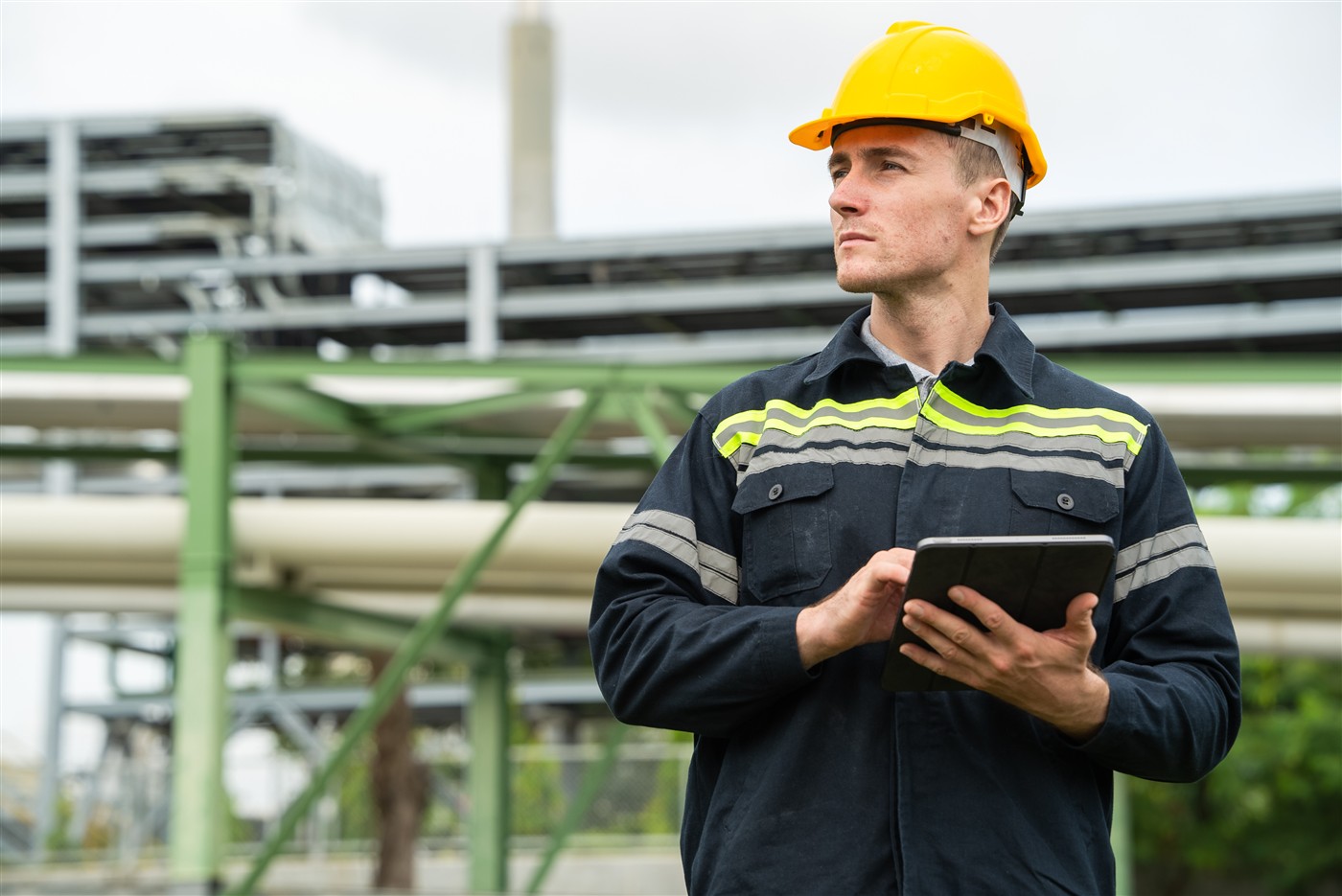 Engineer in hard hat inspecting at a petrochemical facility with tablet